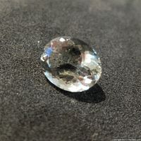 Close-up photo showing round cut faceted green amethyst gemstone with clear transparency and pale green color on black background.