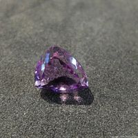 Close-up image of the faceted purple amethyst gemstone on a dark background displaying its triangular shape and faceted cut.