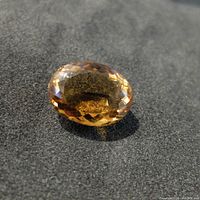 Close-up of the oval faceted citrine gemstone on a dark surface under bright lighting showing the gemstone's cut and color.