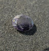 Close-up of the oval-cut blue sapphire gemstone on a dark textured surface showing its facets and color.
