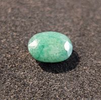 Close-up image of oval cabochon cut emerald gemstone showing green color and surface texture.