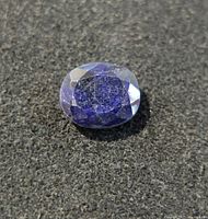Top view of oval-cut blue sapphire showing faceted surface and blue color with inclusions.