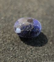 Close-up image of oval blue sapphire showing multiple internal inclusions and surface wear.