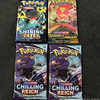 Top view of four sealed Pokémon TCG booster packs: Shining Fates, Darkness Ablaze, and two Chilling Reign packs.