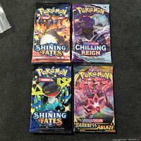 Front view of four sealed Pokémon TCG booster packs featuring Charizard, Dragapult, Toxtricity, and Cinderace artwork