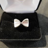 Front view of the sterling silver bow tie ring showing the symmetrical bow tie design, placed in a black velvet ring holder inside a white jewelry box.