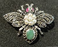 Close-up front view of the sterling silver butterfly brooch showing rubies for eyes, pearls on thorax, and emerald on abdomen.