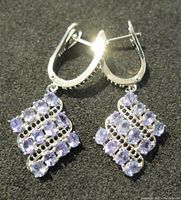 Pair of sterling silver earrings with tanzanite stones laid on a dark surface, showing front view of the earrings.