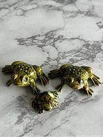 Three vintage porcelain frog figurines on a gray marble surface, showing size and color detail