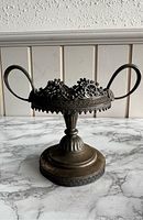 Front view of antique silver plated pedestal bowl showing detailed filigree work and two large handles on a rounded pedestal base