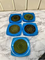 Five vintage blue acrylic coasters arranged on a marble surface showing circular green concentric inset patterns.