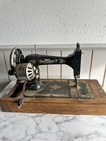 Side view of the sewing machine showing the Greyhound branding and decorative gold detailing on a black metal body mounted on a wooden base.