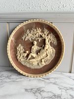 Full view of the circular cameo plate with two reclining figures under a tree, on a marble surface.