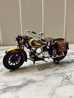 Side angle view of the detailed Indian Sport Scout 1/12 scale motorcycle model showing yellow and brown paint, front wheel, chrome handlebars, and brown saddlebags.