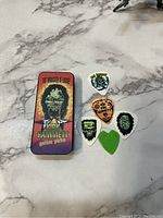 Close-up of Kirk Hammett guitar picks and the collectible tin on a marble surface
