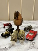 Photo of a wooden egg in a wooden goblet holder surrounded by four toy cars and five animal figurines.
