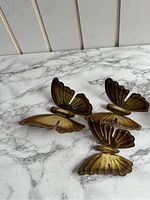 Three gold-colored metal butterfly decorations arranged on a marble surface, showing wing details and build quality.