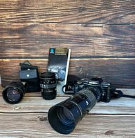 Photo showing Minolta Maximum 7000 camera body, three lenses, camera strap, lens case, and instruction manual on wooden surface.