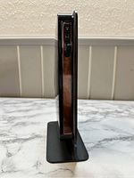 Side view showing slim profile with ports and buttons on the side, standing vertically on black stand.