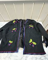 Front view of the black jacket showing blue and red silk trim, and ladybug embroidery with green leaves on chest and lower front.