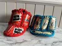 Side view of two handmade crochet party hats, one featuring red crochet and Carling Black Label beer can labels, the other with blue crochet and Coors beer can labels.