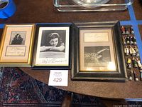 Three framed autographed opera photos and small metal opera character figurines displayed on table.