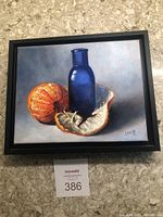 Full front view of framed oil painting showing peeled orange, blue vase and black frame on countertop
