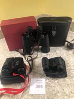 Set of three binoculars and field glasses arranged on a surface, showing the Elite no. 5052 with case and original box, Kinglet 901 with red strap, and unknown model with pouch.