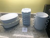 Two white CorningWare oval casserole dishes with lids, six white square dishes stacked with lids, and four white round bowls stacked with handles visible