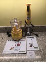 Two yellow Cuisinart kitchen appliances shown together on countertop with power cords and manuals: Mini-Prep Plus food processor with clear bowl and lid, and Smart Stick Hand Blender with clear cup.