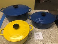 Three enameled cast iron Dutch ovens (large blue oval, medium blue oval, yellow round) on countertop