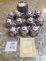 Eleven small covered pots arranged with matching saucers stacked behind, recipe booklet placed in front