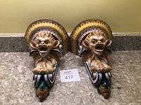 Pair of ceramic gargoyle shelves displayed front-facing on granite counter