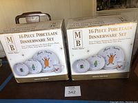 Two original boxes of Merry Brite 16-piece porcelain dinnerware sets shown on a table.