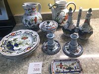 Overview photo showing all ceramic items in the collection including pitchers, plates, oil and vinegar set, candle holders, and trinket dish arranged on kitchen counter.