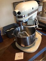 Cream KitchenAid stand mixer on a wooden table with the mixing bowl and attachments inside.
