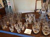 Full set with decanter, ice bucket, shot glasses, tumblers, and tall glasses arranged on table with blue tape.