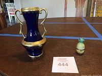Full view of midnight blue and gold urn beside small porcelain pineapple