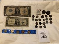 Two worn one-dollar silver certificates and a collection of twenty-one coins including a 1943 steel penny and coins displayed in a blue holder strip.