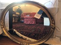 Full view of the 30x25 oval mirror showing its reflective glass and ornate gold tone wood frame with decorative floral elements.