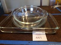 Clear Pyrex and Anchor Hocking glass bakeware dishes stacked on table: one 9x13 baking dish, two 9-inch pie plates, one 1.5-quart open casserole dish