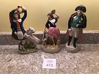 Photo of all three figurines together on granite surface, showing boy with goat, girl with goat, and Napoleon figurine