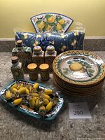 Full view of all lemon-themed kitchen items together including plates, corn holders, bottles, jars, dish, hanging tile, and kitchen towel