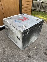 Full view of the metal flight case showing wear, paint scuffs, and 'M' logo on top.