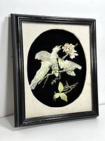 Framed 3D paper art with three white cockatoos on branches against a black oval backdrop, showing the full frame from an angle