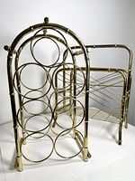 Photo showing vintage brass wine rack with circular holders and brass magazine rack behind it, showing overall condition and design.
