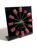 Front view of vintage clock with red dice hour markers mounted on thin gold rods extending from center. Clock hands are gold-tone, and clock face is black square with integrated stand base.