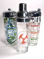 Set of three vintage glass cocktail shakers with shiny metal lids showing different graphics and recipe prints.