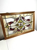 Front of rectangular faux stained glass panel in wooden frame showing red, cream, green colored pattern with black lead imitation lines.