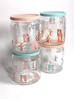 Four vintage glass canisters arranged with two lids on top and two inverted at bottom. Each canister decorated with coral and teal seaweed themed square designs. Lids in matching coral-pink and teal pastel colors.